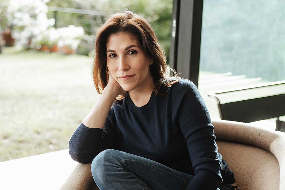 A photograph of Alexandra Lytton Regalado sitting in a chair in front of an open door